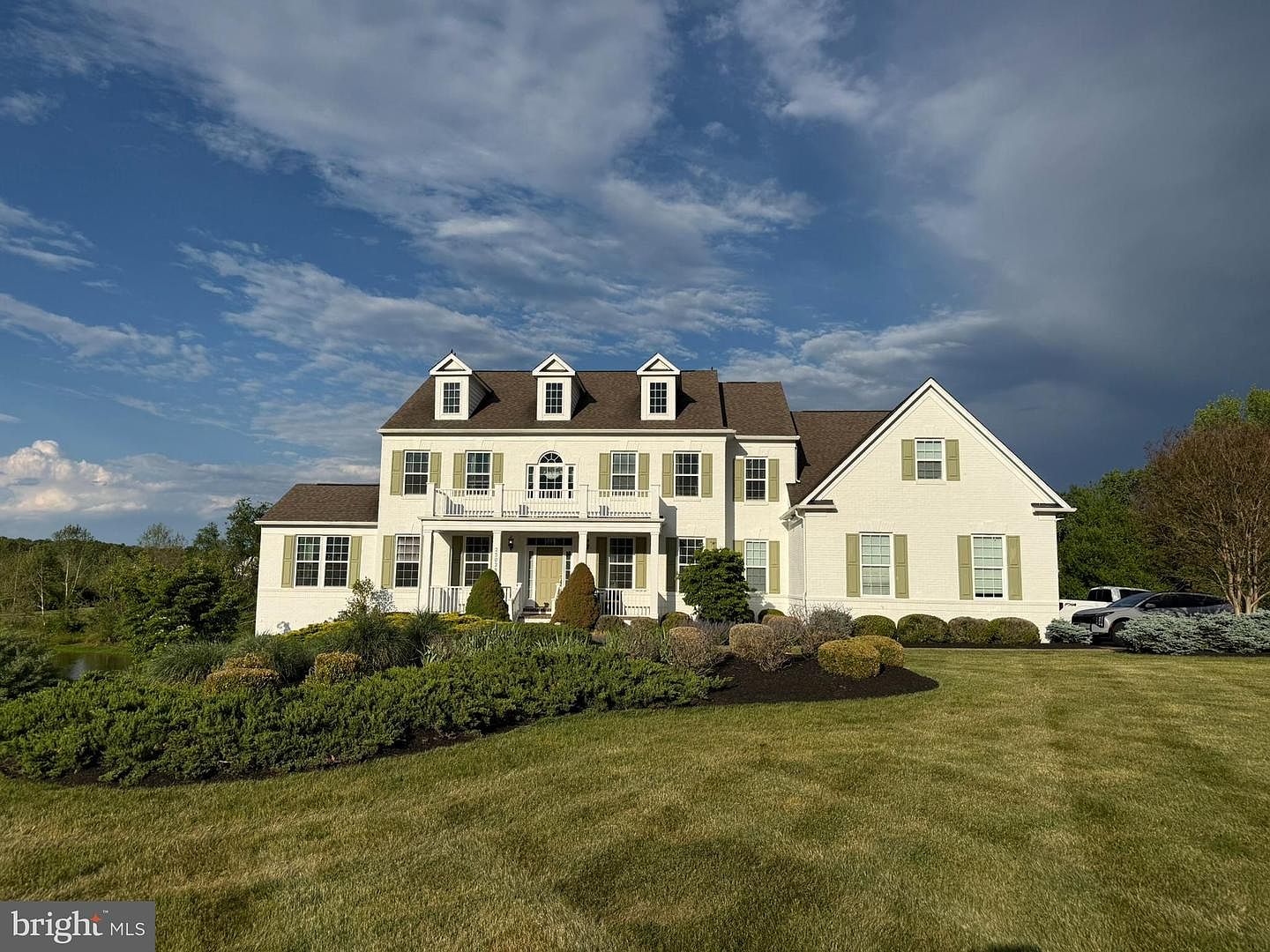 Front elevation of 23028 Creighton Farms Drive, a stately white estate with three dormers and a center entry portico set on a sweeping lawn above a private pond in Leesburg, Virginia